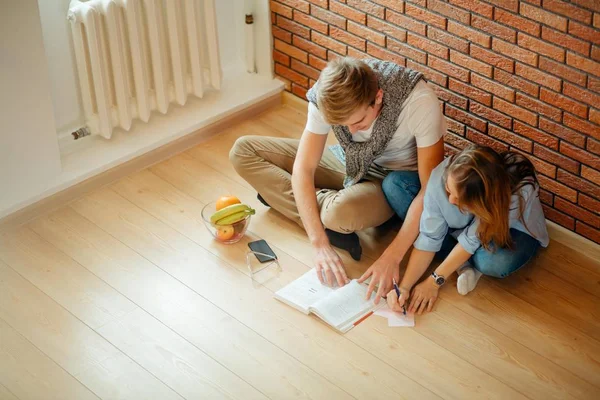 Pareja joven leyendo un libro sentado en el suelo de madera en casa — Foto de Stock