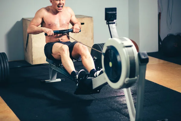 Ajuste o treinamento do homem na máquina da fileira no gym — Fotografia de Stock