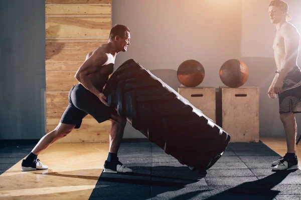 Trainer standing on tire and scream at a man exercising with a tire. — Stock Photo, Image