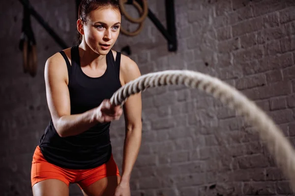 Close up photo of woman doing Battle rope workout near white brick wall — Stock Photo, Image