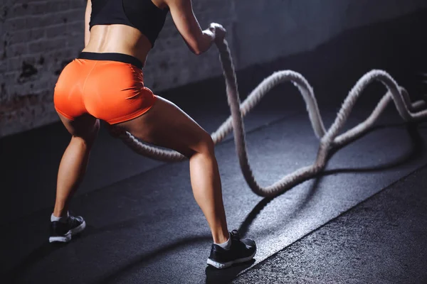 Rear view of tonned woman training with battle rope in cross fit gym — Stock Photo, Image