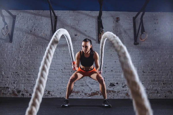 Jovem mulher trabalhando com cordas de batalha em cross fit ginásio — Fotografia de Stock