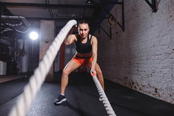 Jovem mulher trabalhando com cordas de batalha em cross fit ginásio — Fotografia de Stock