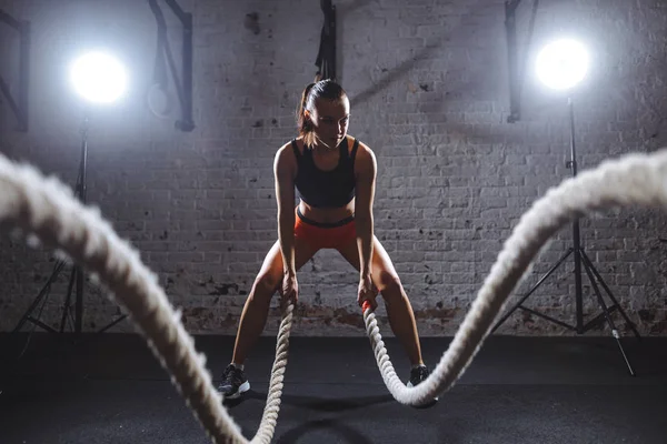 Jovem mulher trabalhando com cordas de batalha em cross fit ginásio — Fotografia de Stock