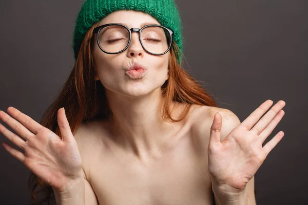 Рыжая женщина в очках и зеленой шляпе надувает губы, готовясь к поцелую — стоковое фото