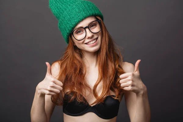 Pelirroja con sujetador negro, gafas y sombrero de punto verde muestran dos pulgares hacia arriba — Foto de Stock