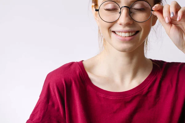 Ruiva sorrindo mulher vestindo camisa vermelha segurar óculos no fundo branco — Fotografia de Stock