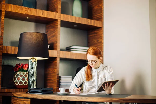 Frau schreibt mit digitalem Tablet-Computer im Büro auf Papier — Stockfoto