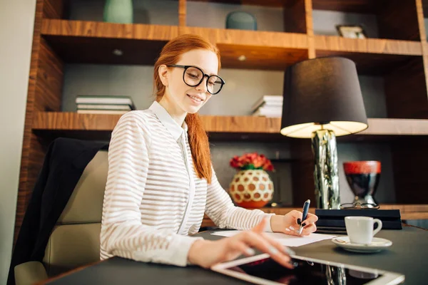 Рыжая улыбающаяся молодая женщина-менеджер, использующая современные цифровые планшеты в офисе — стоковое фото