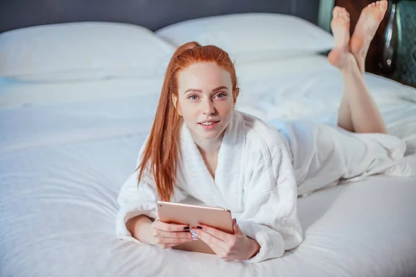 Hermosa mujer con albornoz y el uso de tabletas digitales mientras se relaja en la cama — Foto de Stock