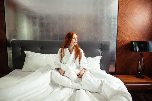 Redhead mladá žena s pihy, sedí na posteli relaxační — Stock fotografie