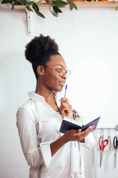 Costurera chica africana tomando notas en el cuaderno. bocetos de dibujo de diseño —  Fotos de Stock