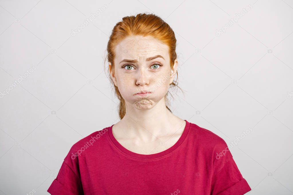 woman with freckles blowing her cheeks, frowning, feeling frustrated