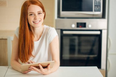 Tablet tutarak ve kameraya bakarak mutlu genç kadın