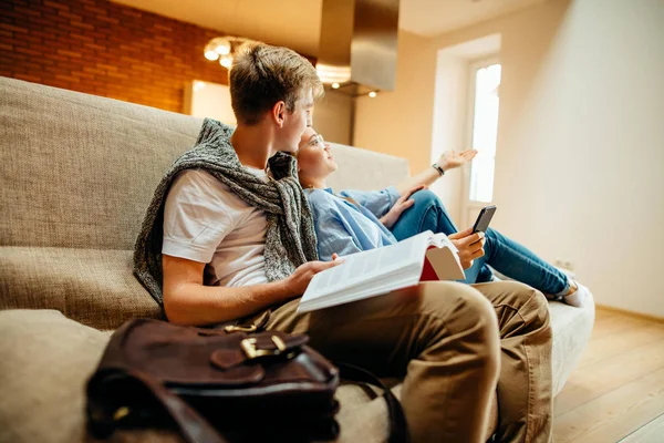 Paar zittend op de Bank, vrije tijd samen, leesboek voor man, vrouw met behulp van de telefoon — Stockfoto