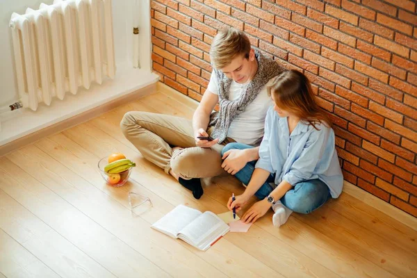 Pareja joven leyendo un libro sentado en el suelo de madera en casa — Foto de Stock