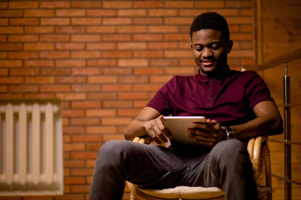 Homem africano usando tablet para conversa em vídeo enquanto relaxa na poltrona — Fotografia de Stock