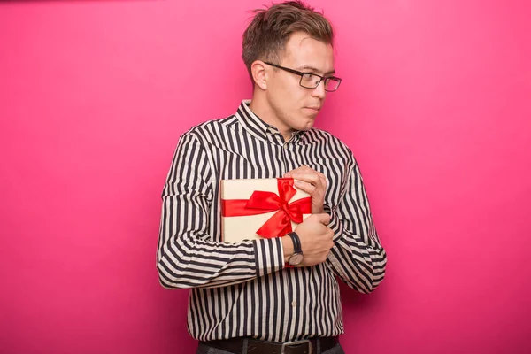 Glücklicher junger Mann mit einem dekorativen Geschenk auf rosa Hintergrund — Stockfoto