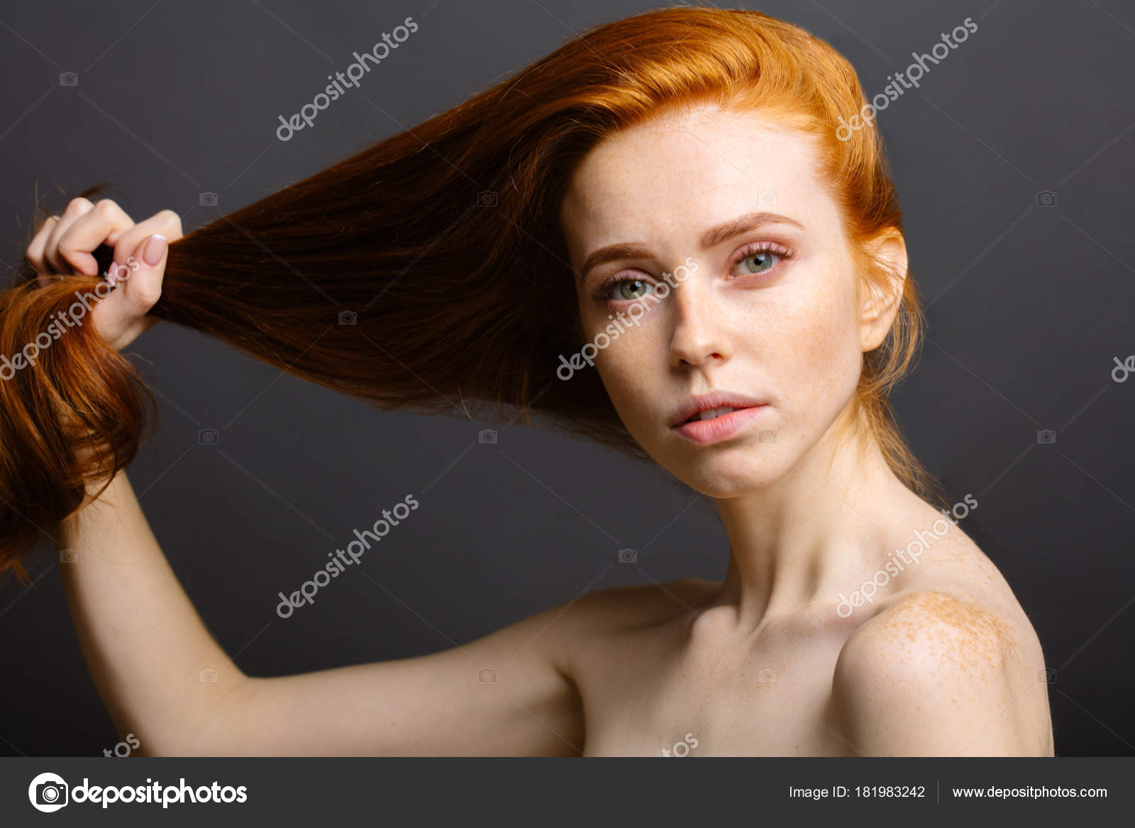 Gorgeous young woman with long red hair and strapless bra pulling back in  ponytail over black background. Healthy Hair and Skin Care Stock Photo