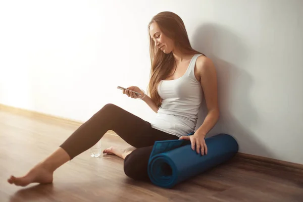 Mujer haciendo yoga y usando el teléfono celular sentado en el suelo — Foto de Stock