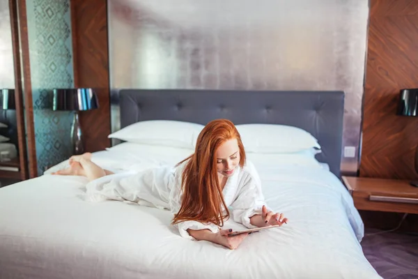 Hermosa mujer con albornoz y el uso de tabletas digitales mientras se relaja en la cama — Foto de Stock