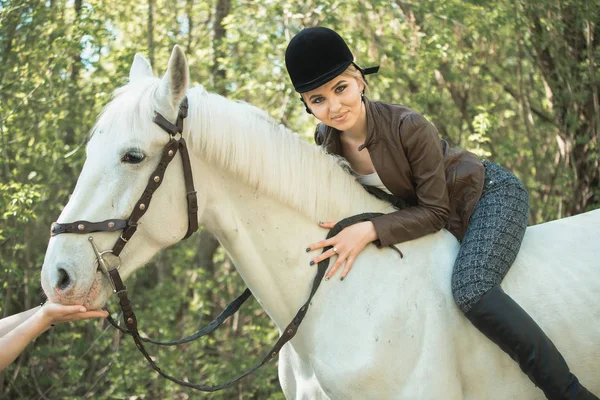 Brunette woman riding dark horse at summer green forest. — Stock Photo, Image