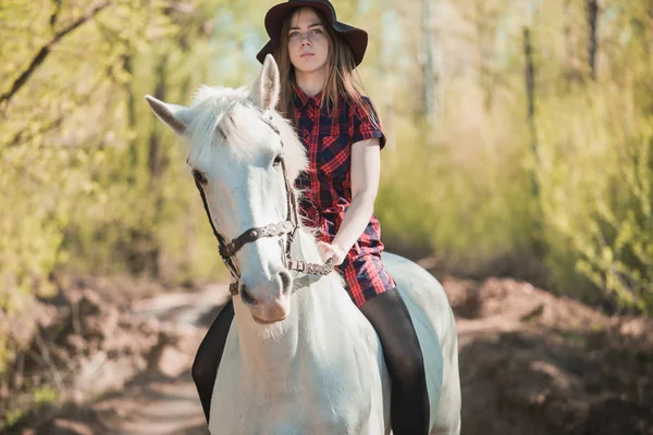 Brunette woman riding dark horse at summer green forest. — Stock Photo, Image