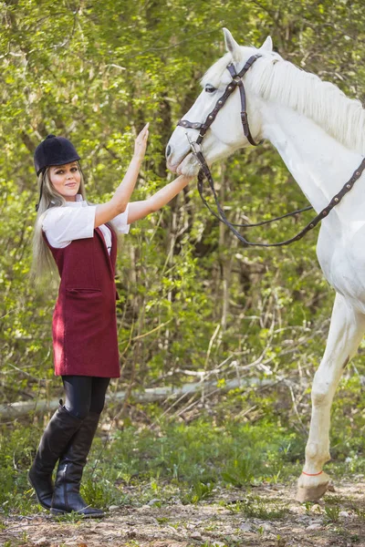 Hermosa chica morena con el pelo largo posando con un caballo rojo en el bosque — Foto de Stock