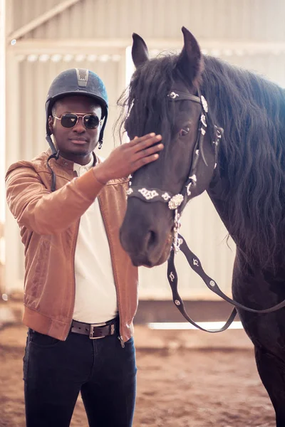 African Man wearing sunglasses near black horse in hangar — Stock Photo, Image