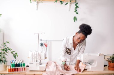 Gülümseyen terzi dikiş makinesiyle kameraya bakıyor.