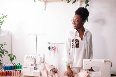 Gülümseyen terzi dikiş makinesiyle kameraya bakıyor.