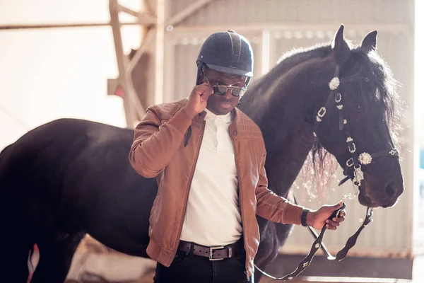 African Man wearing sunglasses near black horse in hangar — Stock Photo, Image