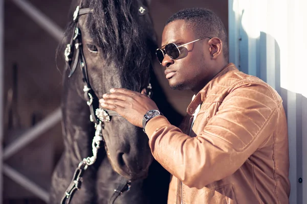 Afrikaner mit Sonnenbrille in der Nähe eines schwarzen Pferdes im Hangar — Stockfoto