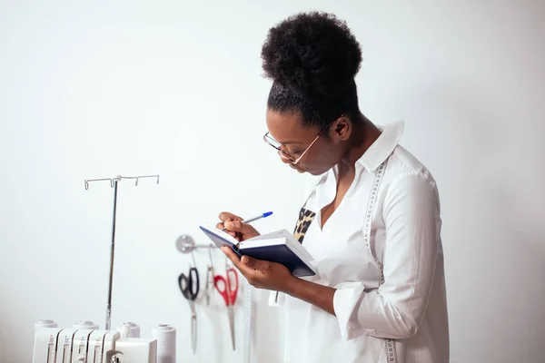 Afrikanische Näherin, die Notizen am Notizbuch macht. Designer zeichnen Skizzen — Stockfoto