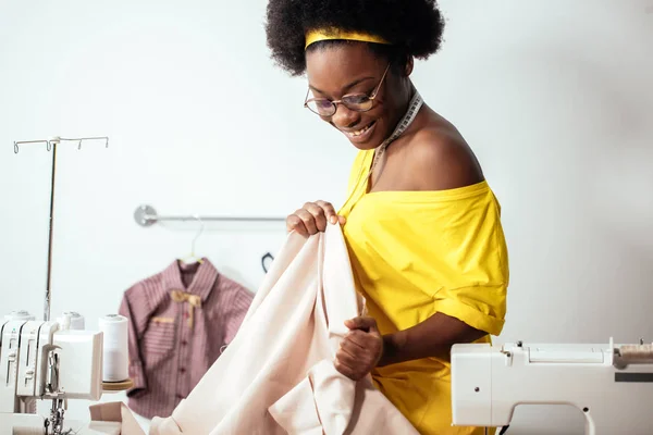 Afrikkalainen nainen ompelija katselee vaaleanpunaisia kankaita ja seisoo työpajassa — kuvapankkivalokuva