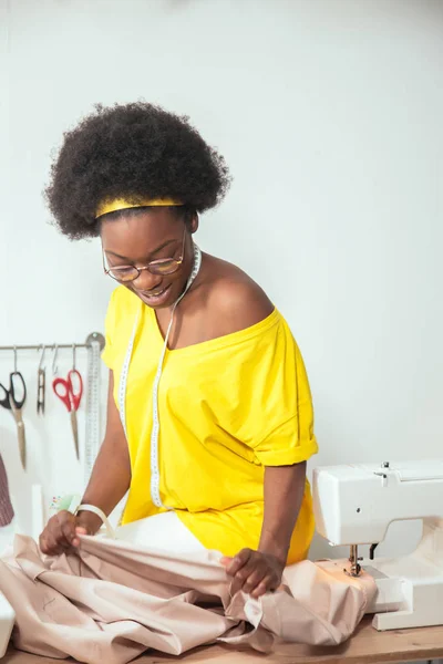 Африканская женщина швея глядя на розовые ткани и стоя в мастерской — стоковое фото