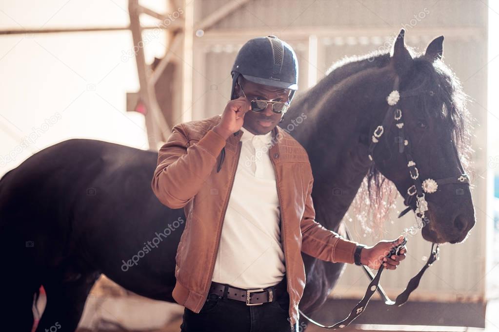 african Man wearing sunglasses near black horse in hangar