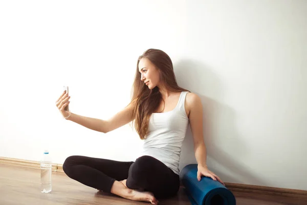 Mujer sentada en el suelo y haciendo selfie en el teléfono inteligente en el gimnasio — Foto de Stock