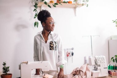 Gülümseyen terzi dikiş makinesiyle kameraya bakıyor.