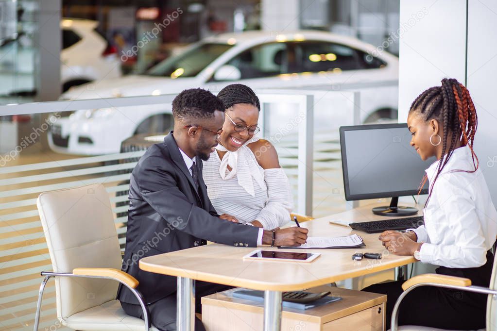 african couple getting car key from dealer in showroom and signing contract