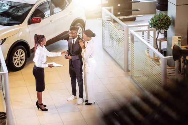 Autoverkäufer steht im Autohaus und erzählt Kunden von Merkmalen des Autos — Stockfoto