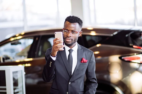 african car salesman using smart phone in showroom