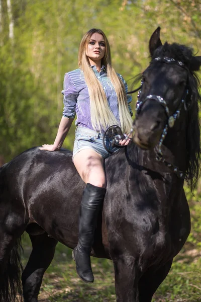 Brünette Frau reitet dunkles Pferd im sommergrünen Wald. — Stockfoto