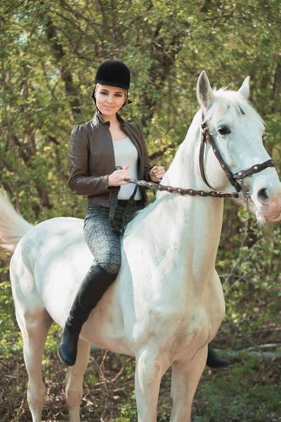 Brunette woman riding dark horse at summer green forest. — Stock Photo, Image