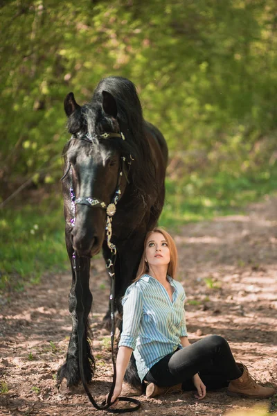 Mujer guapa sentada en el suelo con caballo marrón cerca de ella . — Foto de Stock