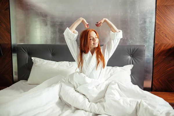 Rothaarige Frau dehnt sich nach dem Aufwachen im Bett — Stockfoto