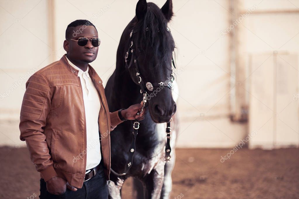 african Man wearing sunglasses near black horse in hangar