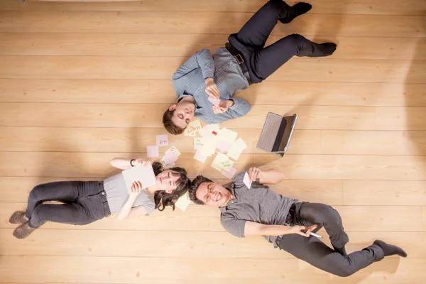 Вид сверху три студента улыбаются в камеру, лежа на деревянном полу — стоковое фото