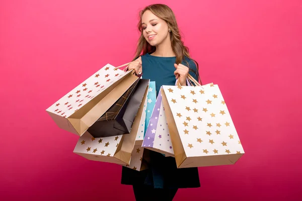 Κορίτσι, κρατώντας τσάντες για ψώνια και να βλέπουν τα φωτογραφικών μηχανών που απομονώνονται σε ροζ φόντο — Φωτογραφία Αρχείου