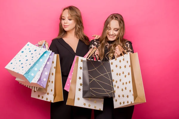 Meninas estão segurando sacos de compras, sorrindo enquanto está de pé no fundo rosa — Fotografia de Stock